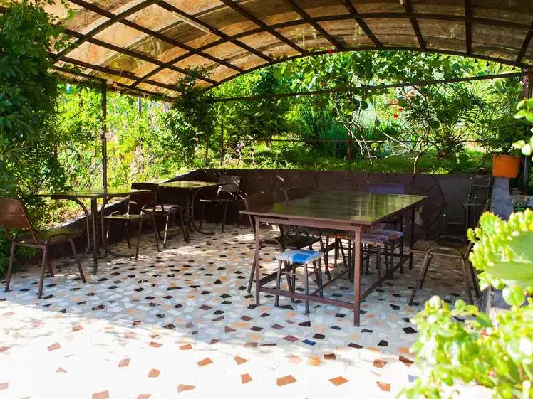 Большая крытая беседка со столиками. На шпалере несколько деревьев киви. В беседке есть освещение и розетка